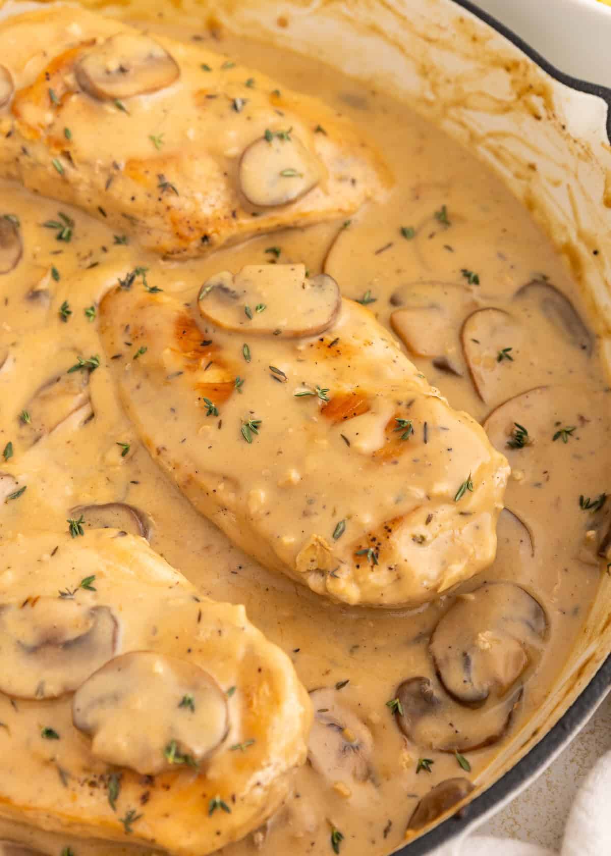 Chicken breasts in creamy mushroom sauce, garnished with herbs, in a skillet.