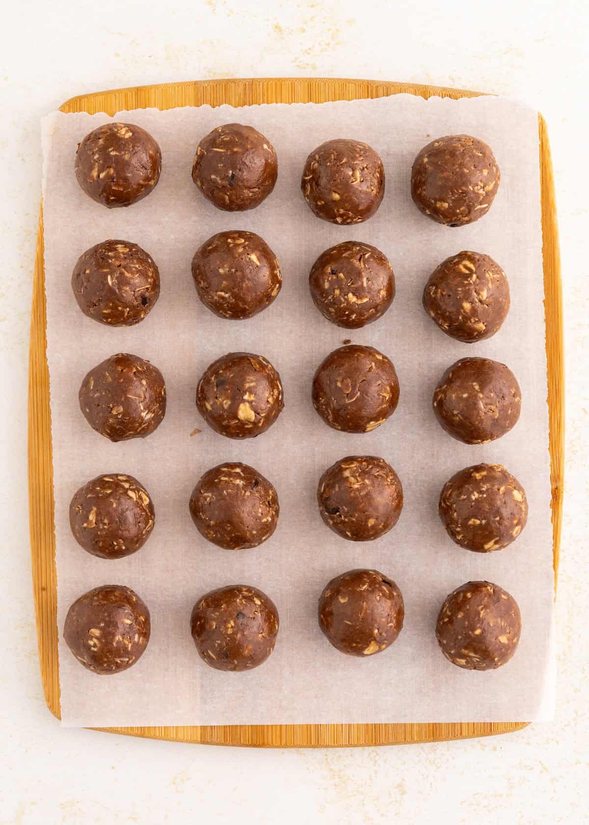 Twenty chocolate energy balls arranged in rows on parchment paper over a wooden board.