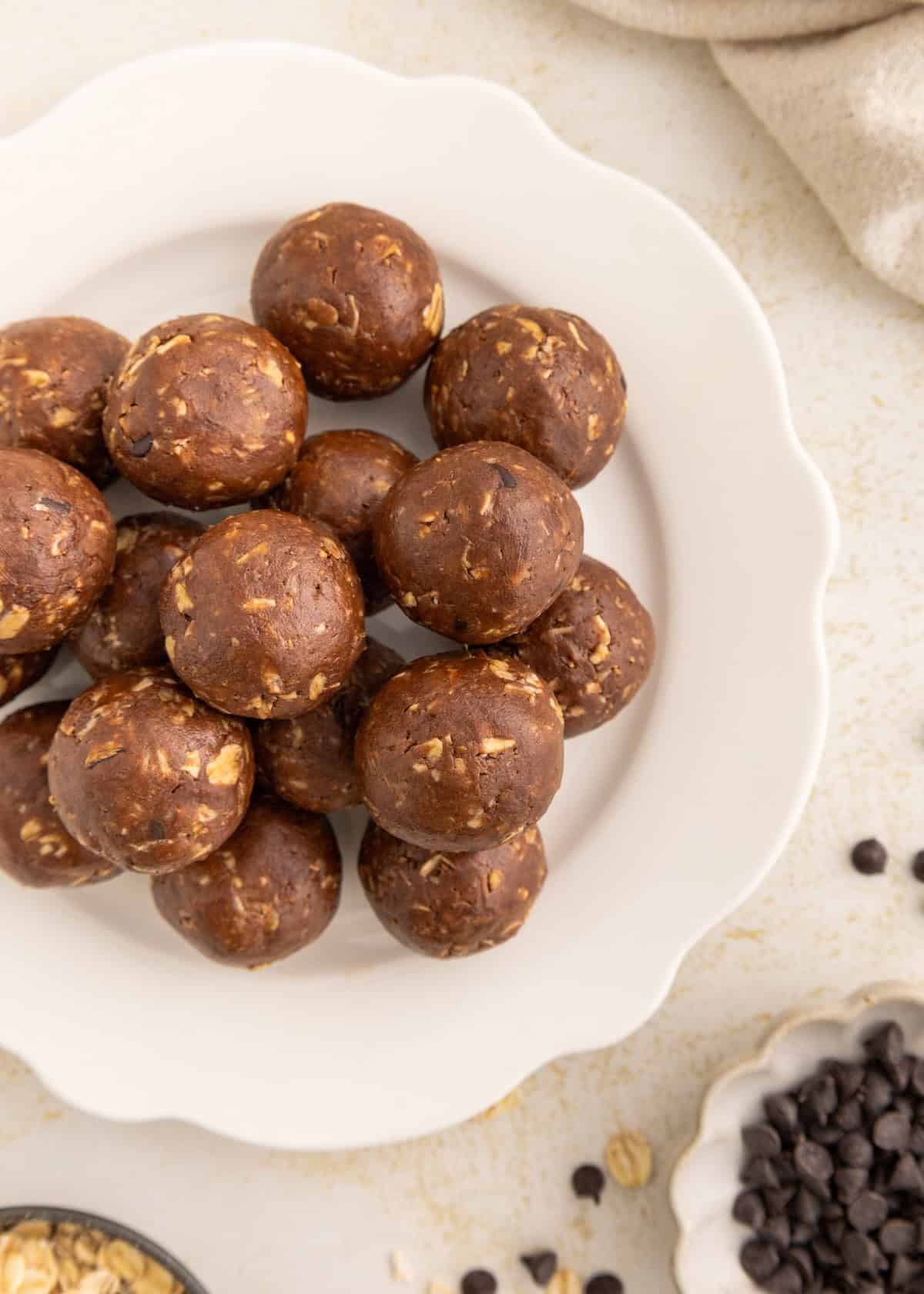 A plate of chocolate oat energy balls on a white plate, with chocolate chips nearby.