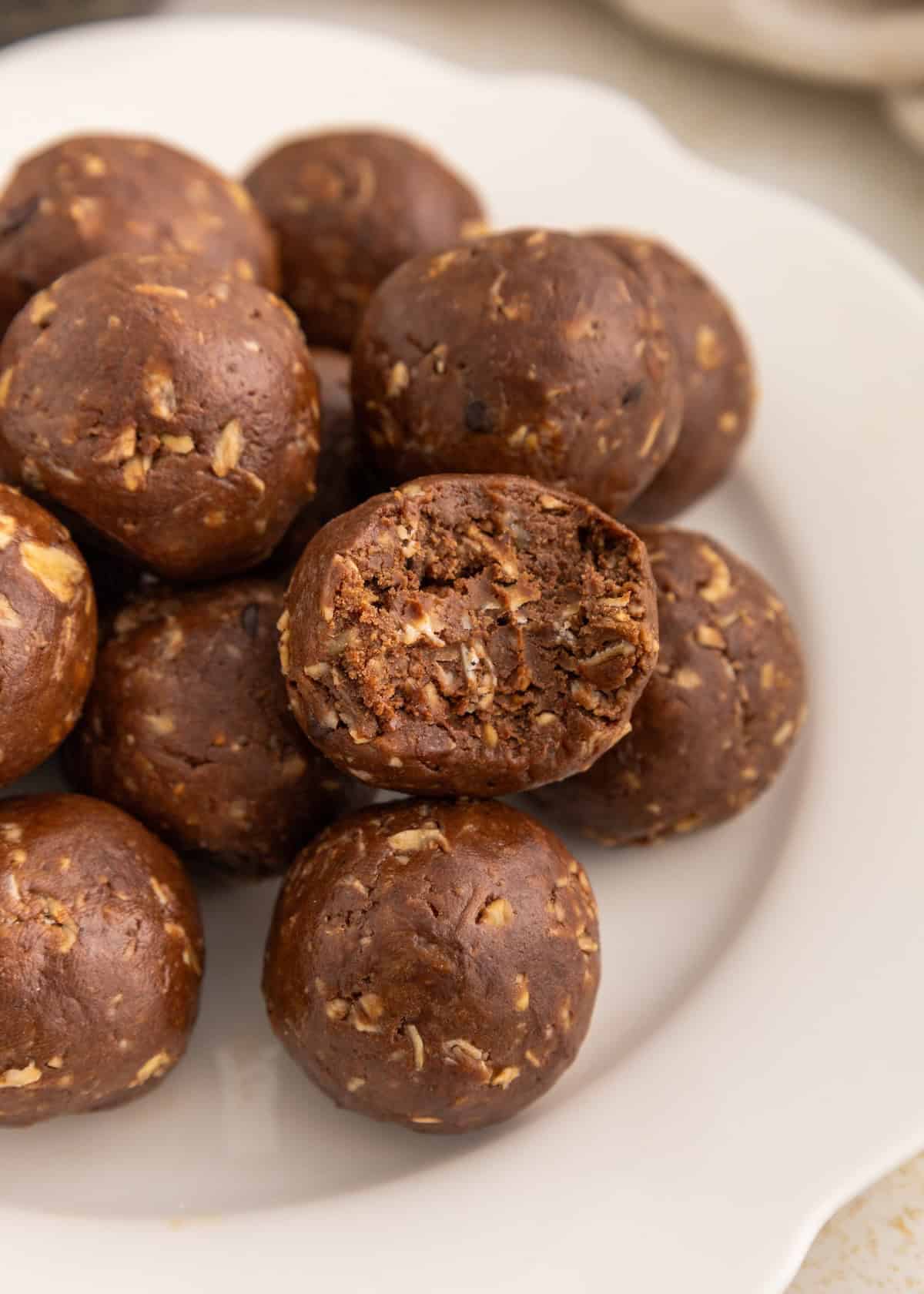 Chocolate oat energy balls on a white plate, with one showing a bite taken out.