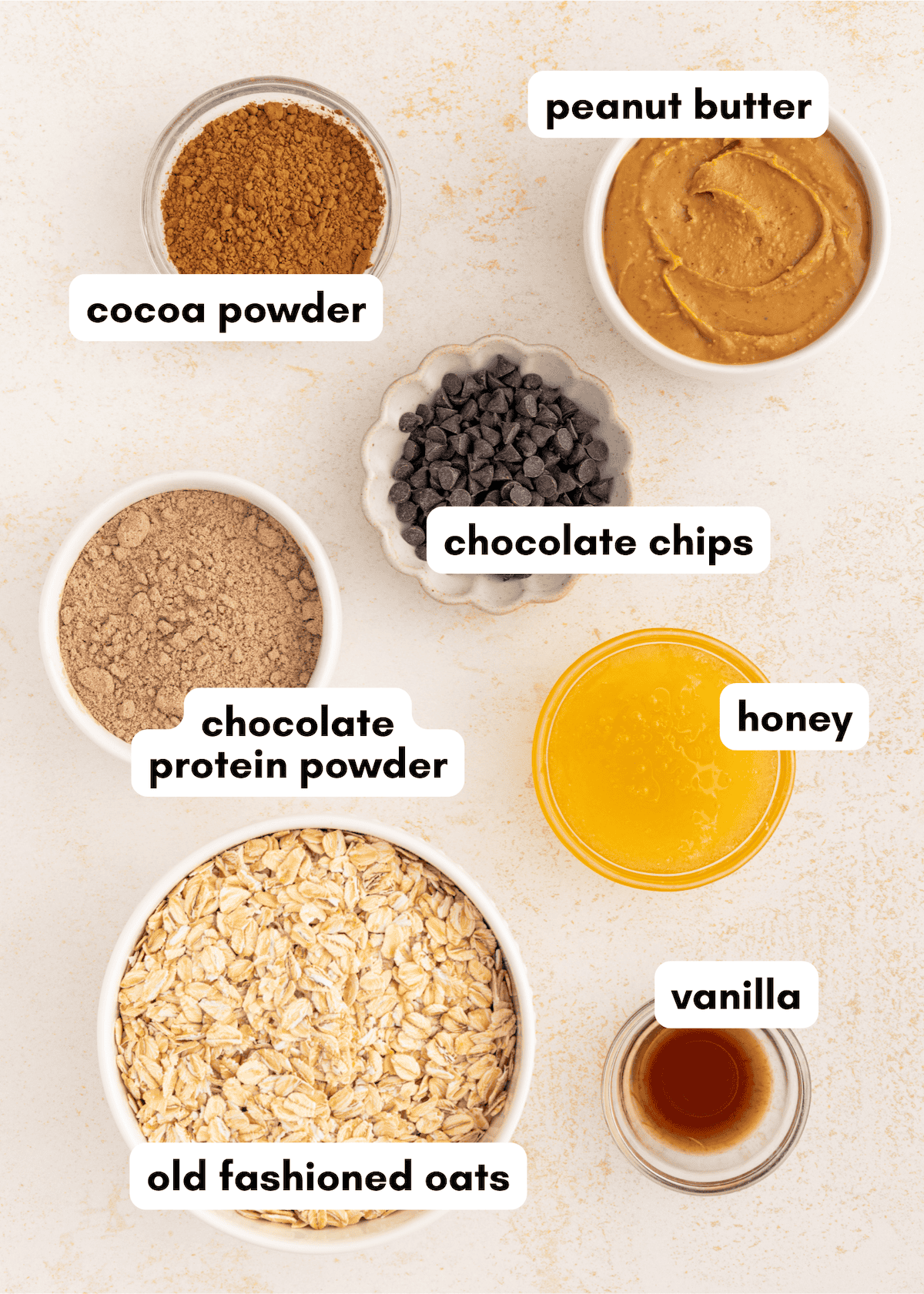 Bowls with labeled ingredients: cocoa powder, oats, protein powder, peanut butter, honey, vanilla, chips.