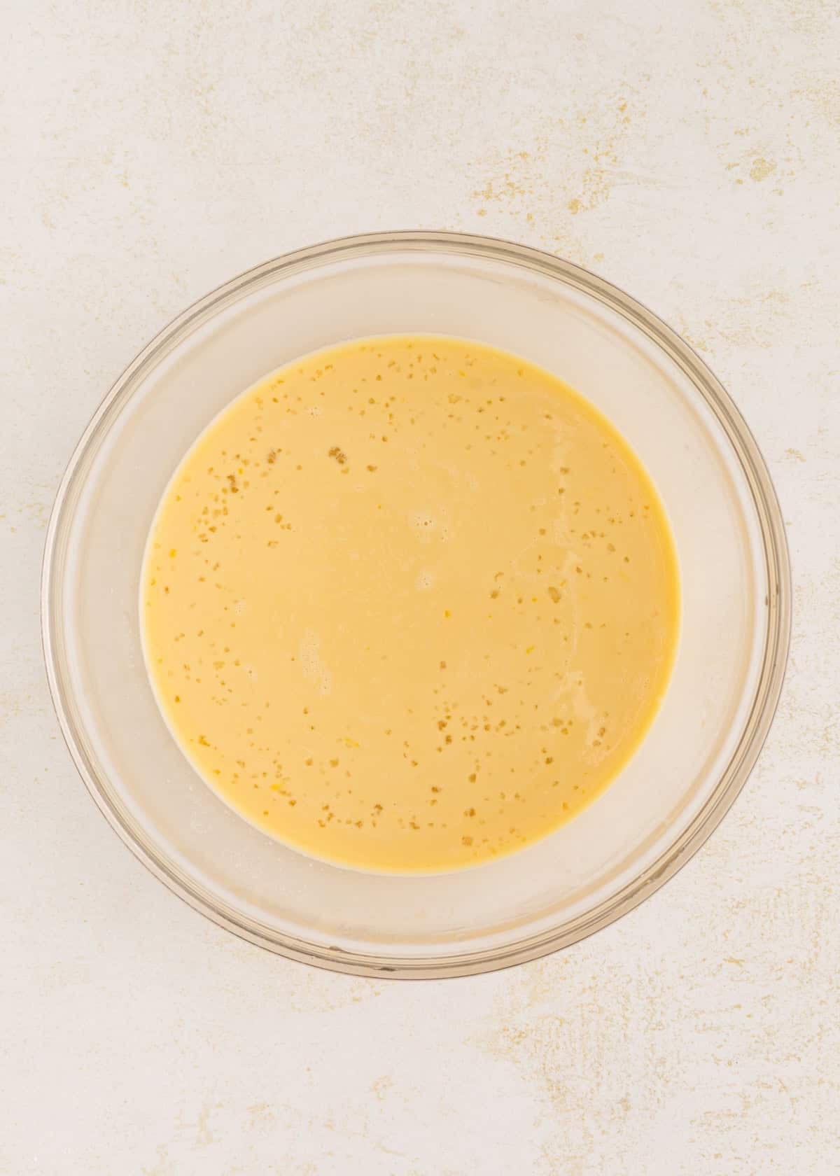 A glass bowl filled with a yellow liquid mixture on a light-colored surface.