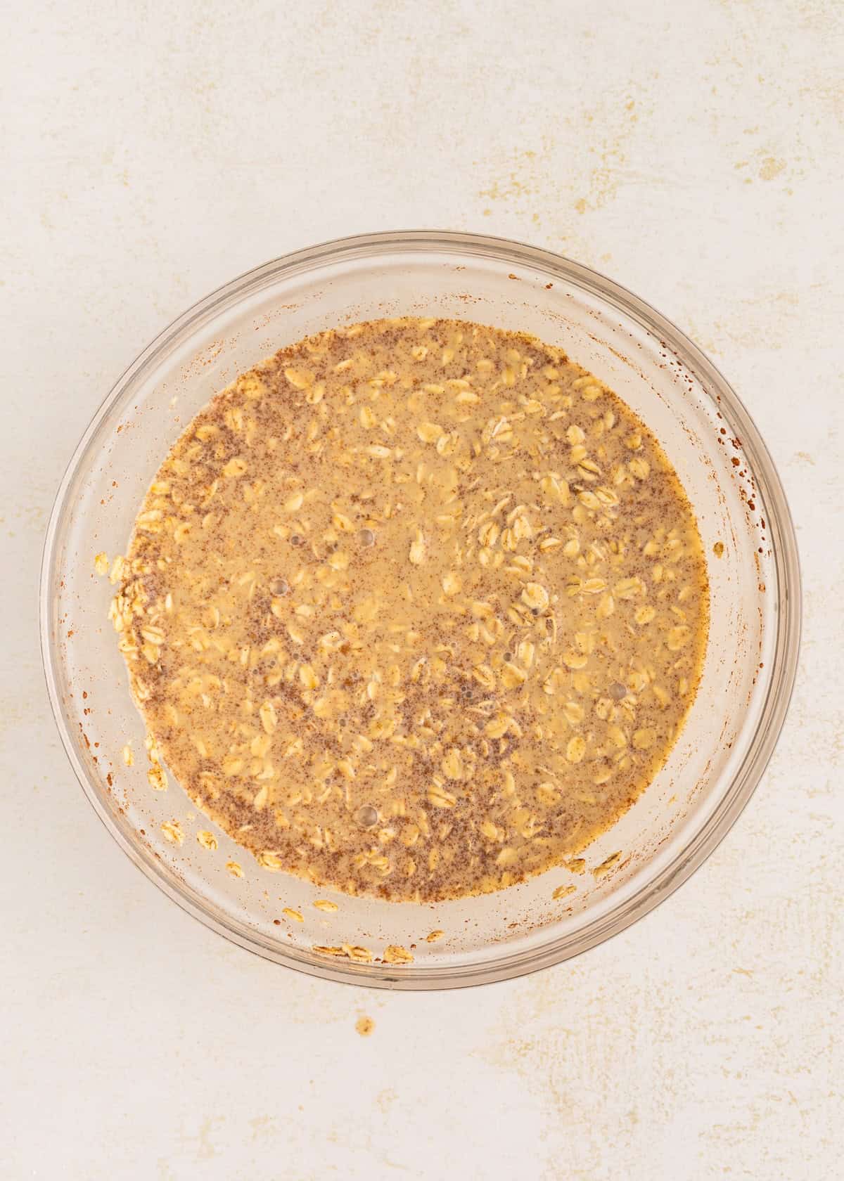 A glass bowl filled with a mixture of oats and liquid on a light surface.