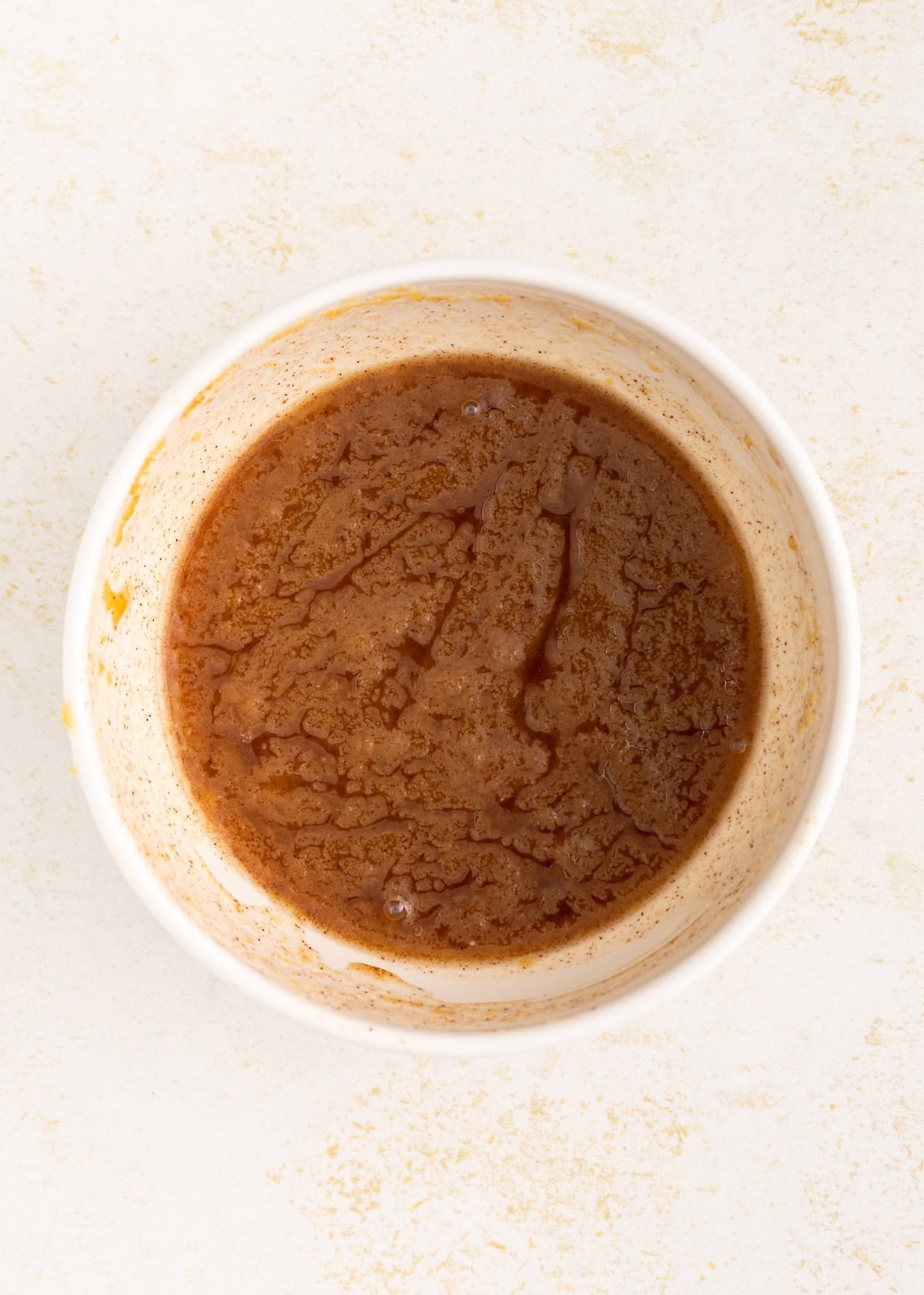 Brown liquid seasoning or sauce in a white bowl, seen from above on a light surface.