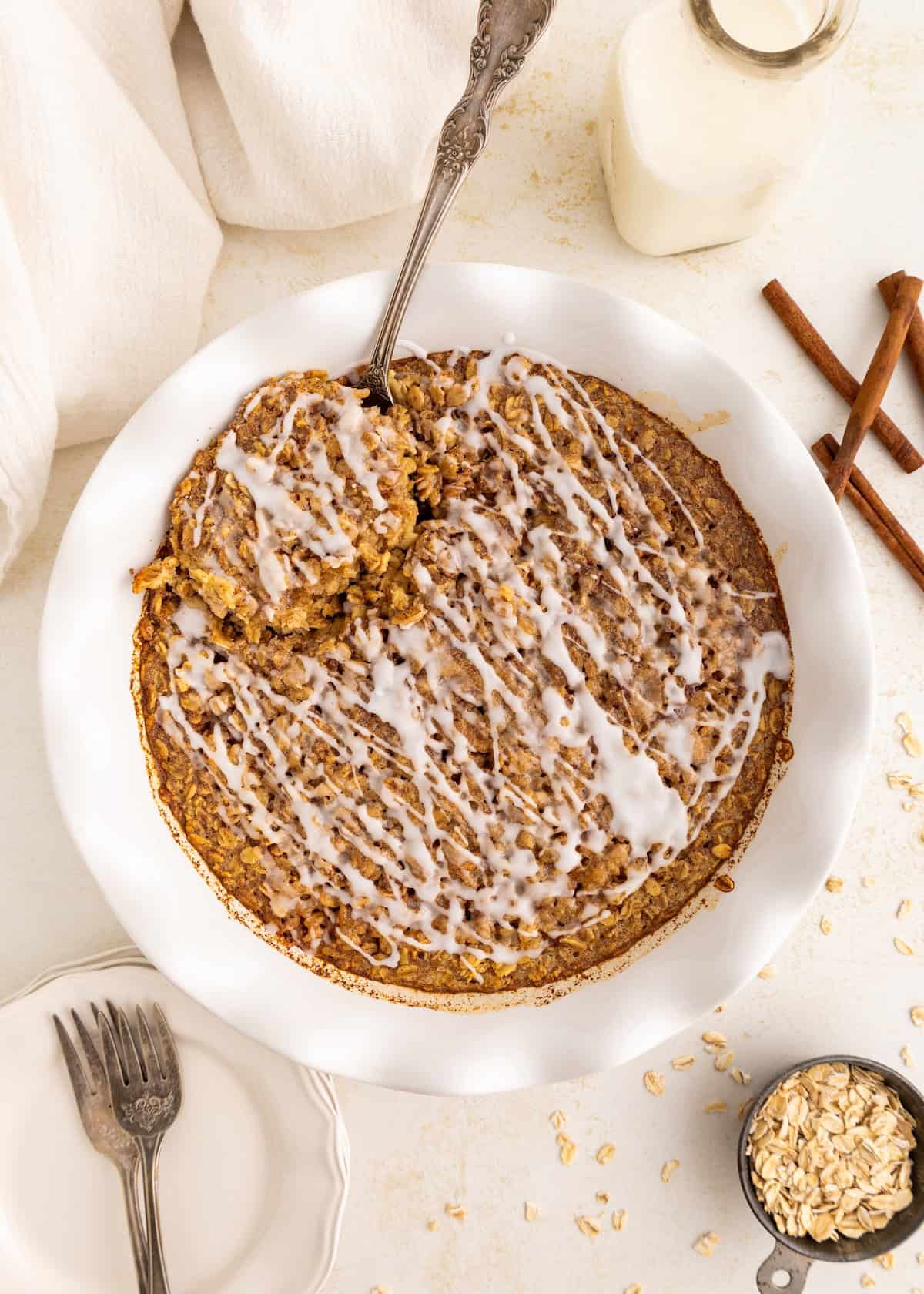 Baked oatmeal drizzled with icing in a white dish, with a spoon and milk nearby.