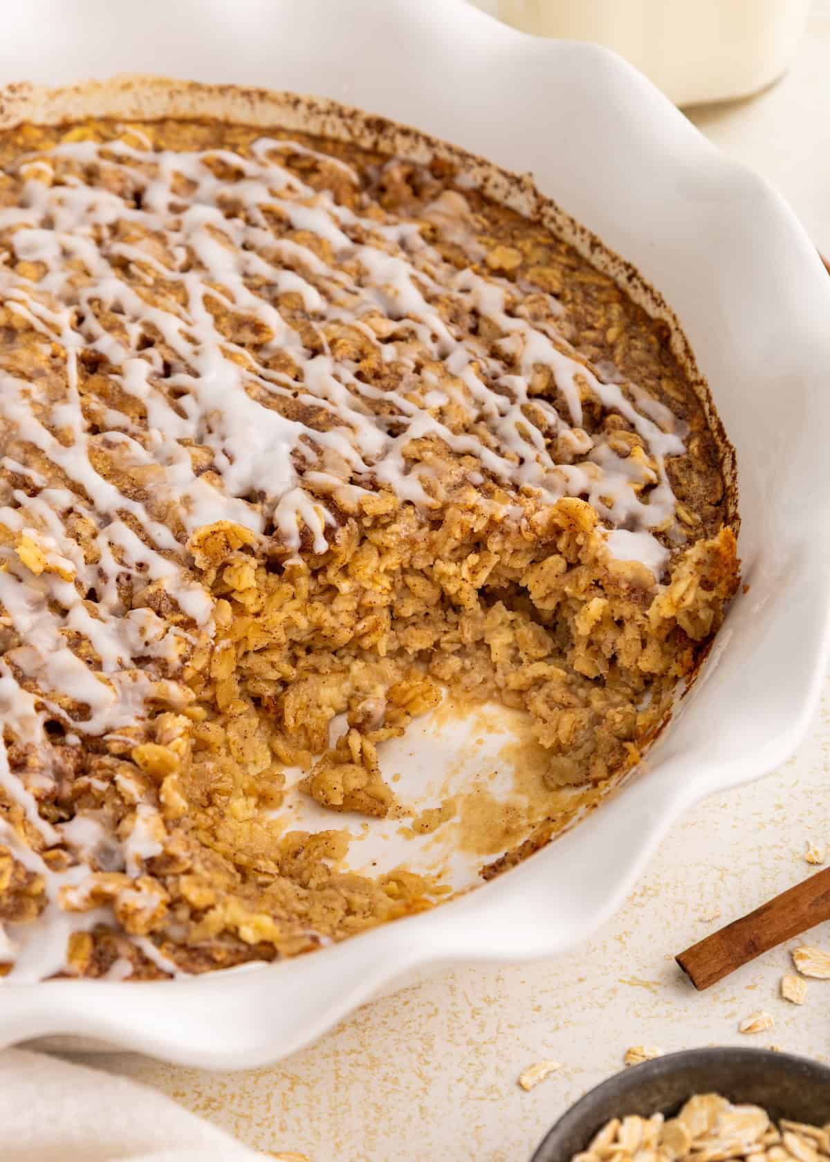 Baked oatmeal in a white dish with icing drizzled on top and a portion scooped out.
