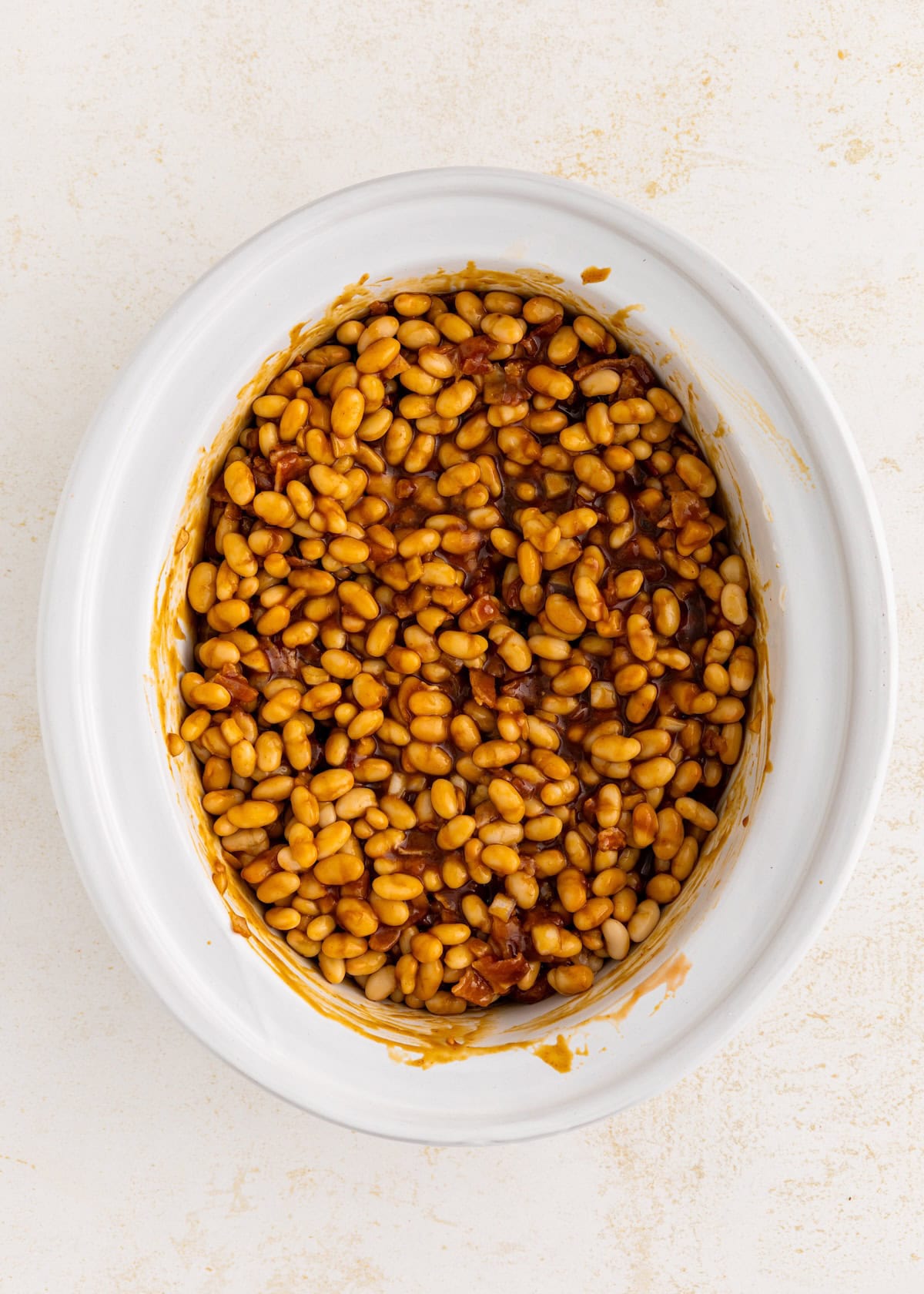 White oval dish filled with baked beans in sauce, seen from above on a light background.