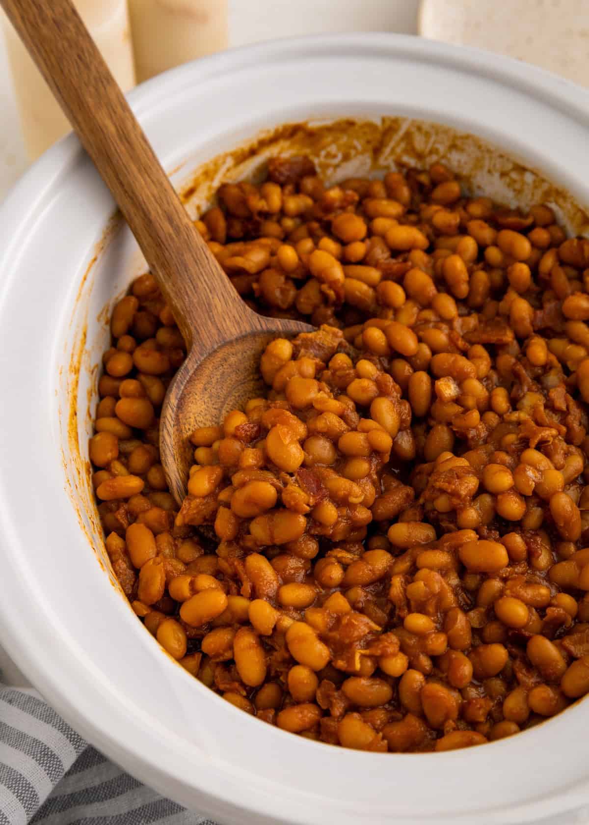 Baked beans in a white dish with a wooden spoon, ready to serve.