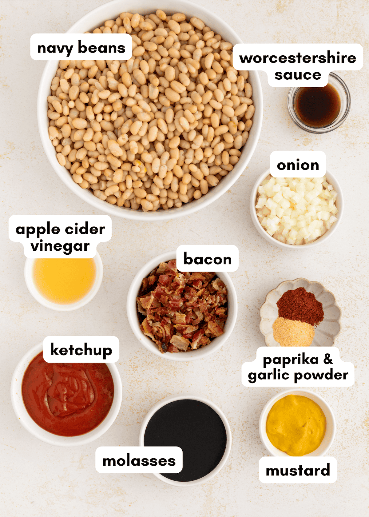 Bowls with navy beans, bacon, onion, ketchup, molasses, vinegar, sauce, spices, and mustard.