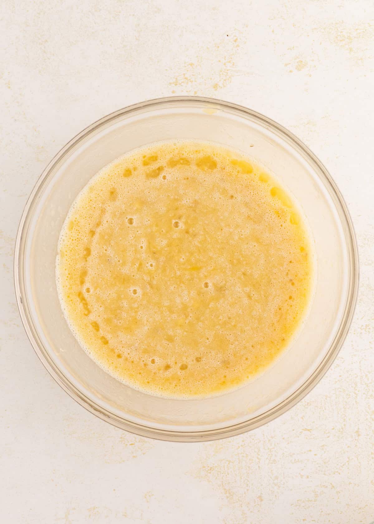 A bubbly, yellow batter is in a clear glass bowl.