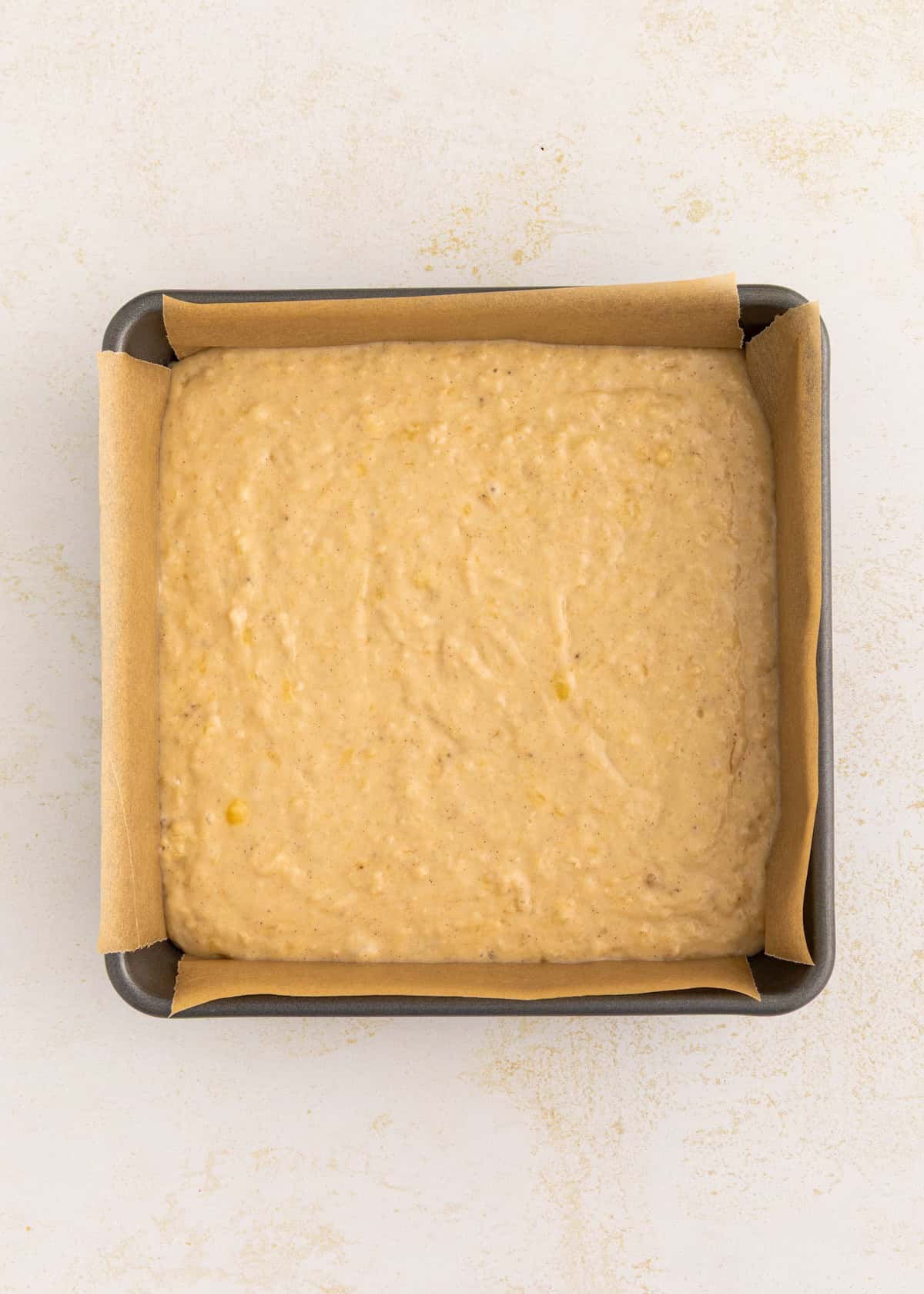 Banana bread batter in a square baking pan lined with parchment paper.