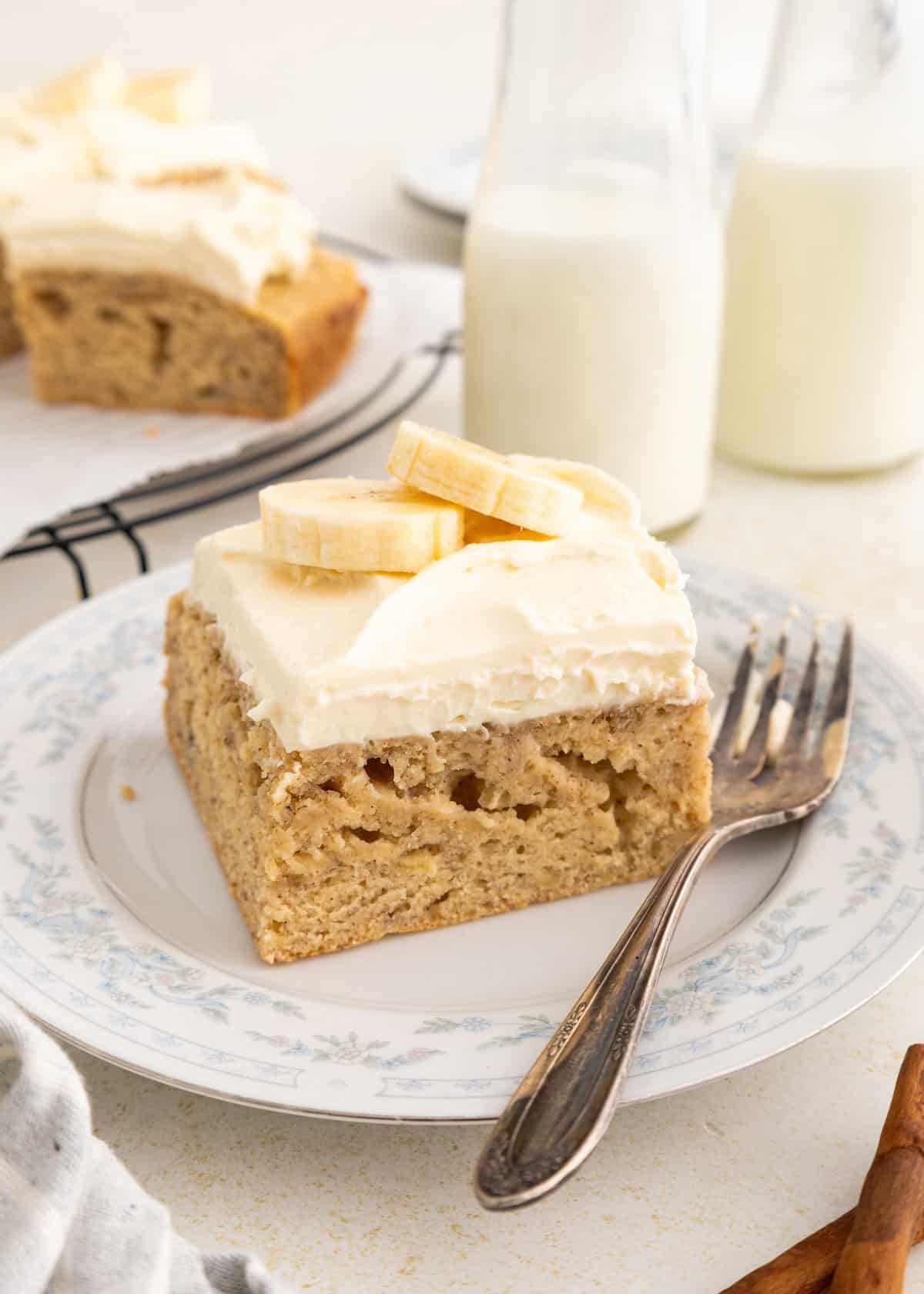 Slice of banana cake with cream cheese frosting and sliced bananas.