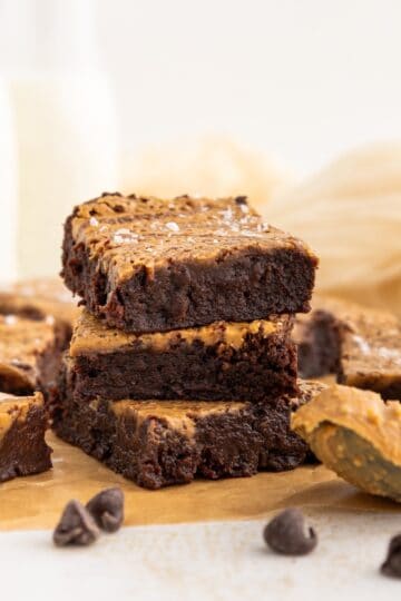 Three chocolate brownies with a peanut butter swirl stacked on parchment paper, with chocolate chips.