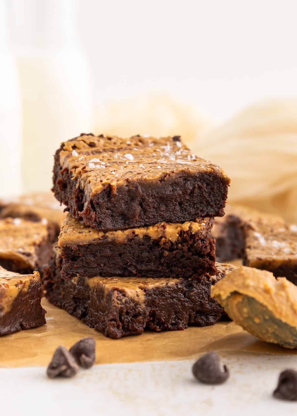Three chocolate brownies with a peanut butter swirl stacked on parchment paper, with chocolate chips.