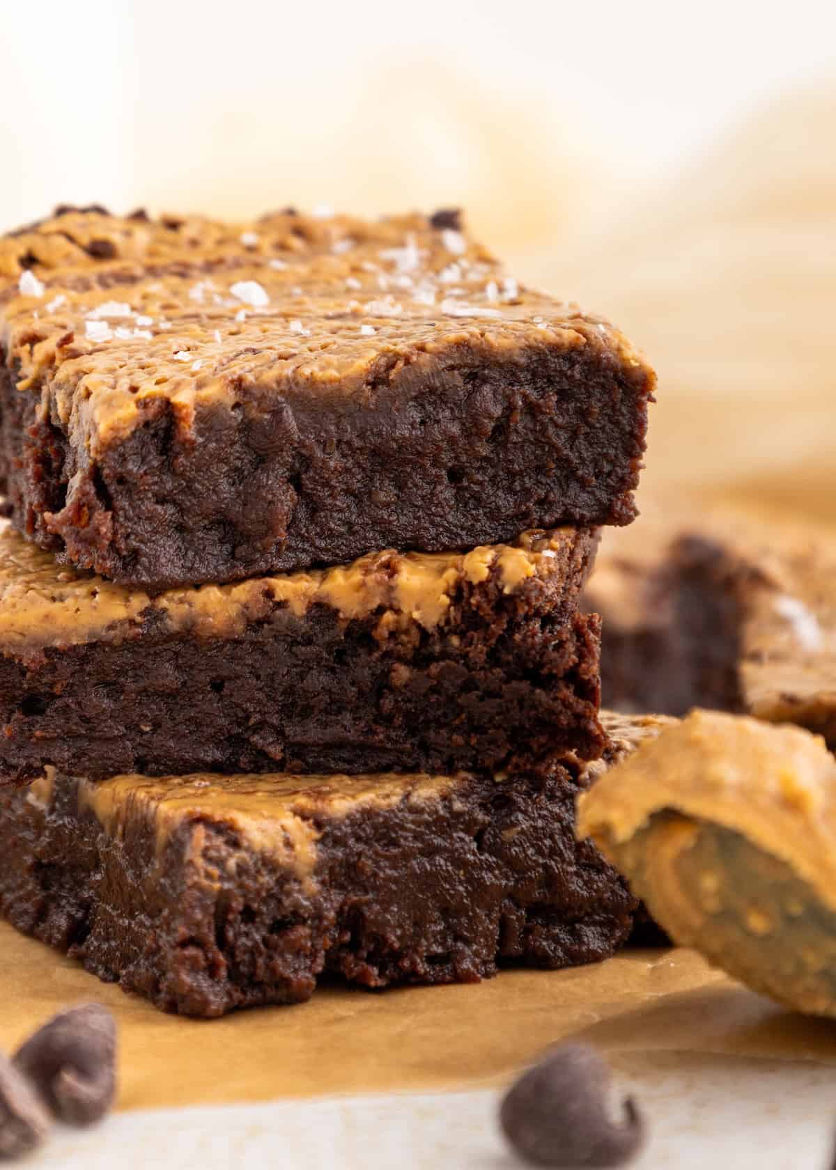 Stack of fudgy brownies with a swirl of peanut butter on top, resting on parchment paper.