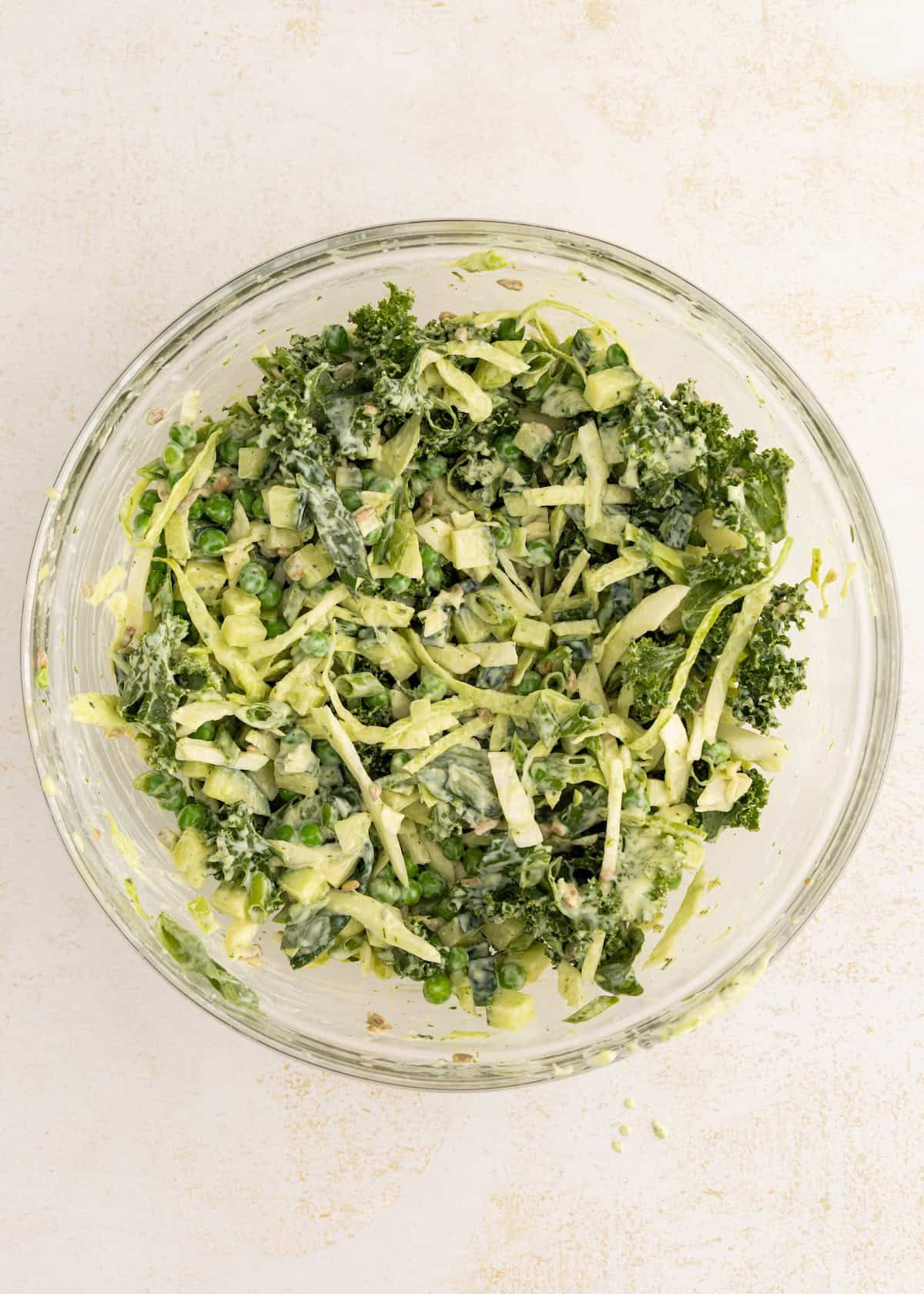 A glass bowl filled with creamy green salad on a light background.