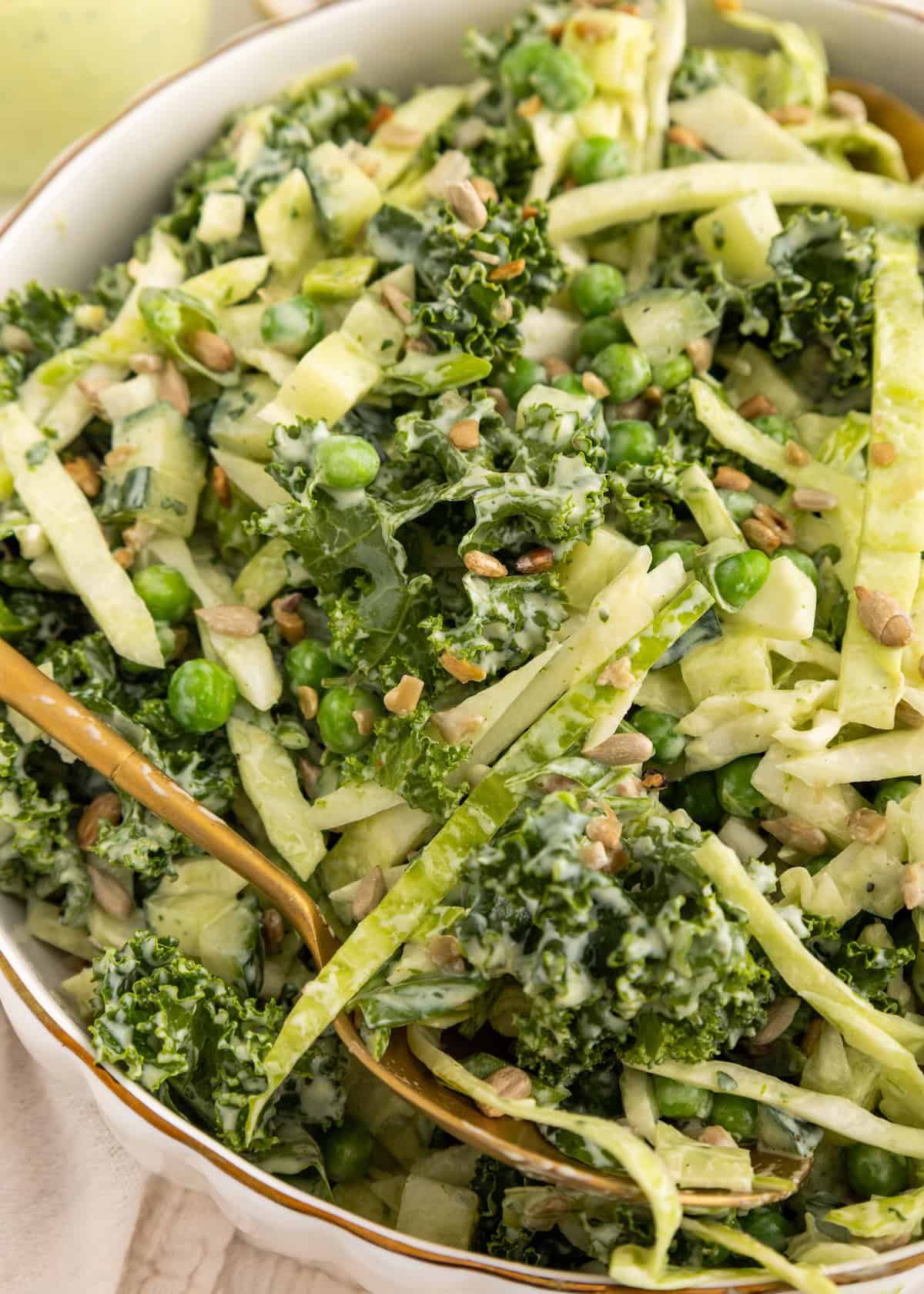 A close-up of a green salad with kale, peas, sunflower seeds, and creamy dressing.