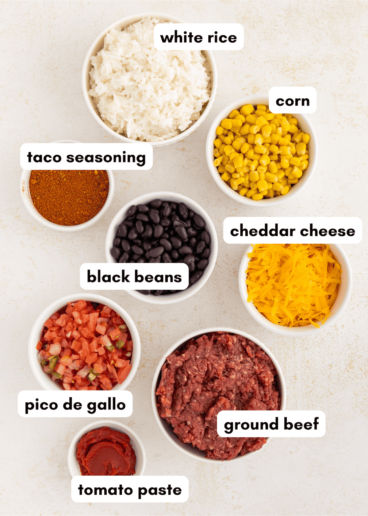 Bowls of white rice, corn, taco seasoning, black beans, cheddar cheese, pico de gallo, ground beef, and tomato paste.