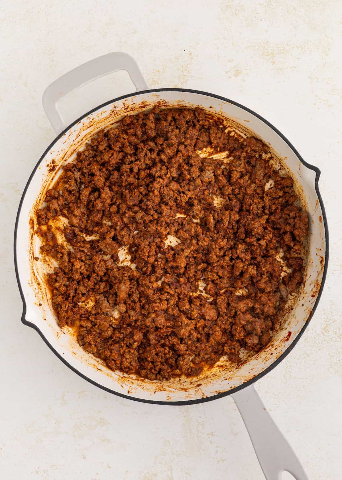 Cooked ground beef with seasoning in a white pot on a light surface.