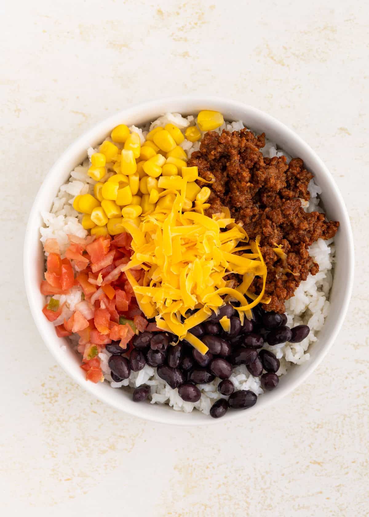 Bowl with rice, ground meat, black beans, corn, diced tomatoes, and shredded cheese.
