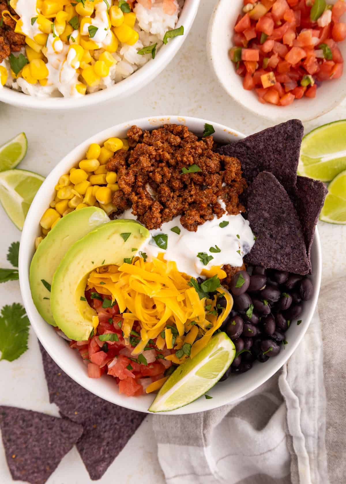 Burrito bowl with ground beef, avocado, black beans, corn, cheese, sour cream, and blue chips.