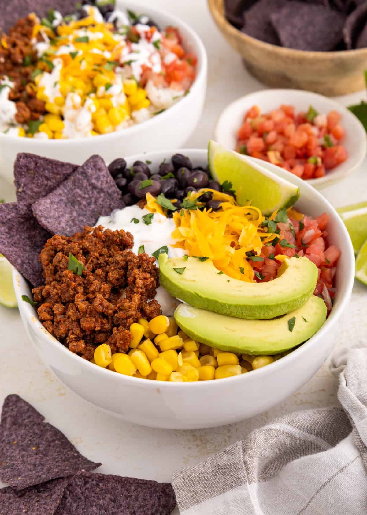A burrito bowl with avocado, corn, ground meat, black beans, chips, and cheese.