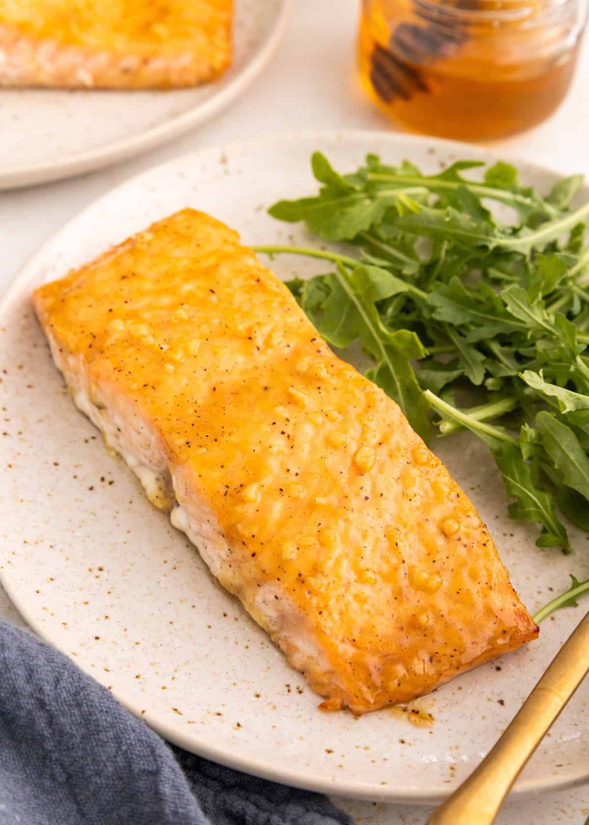 Baked salmon fillet with arugula salad on a plate, next to a jar of honey.