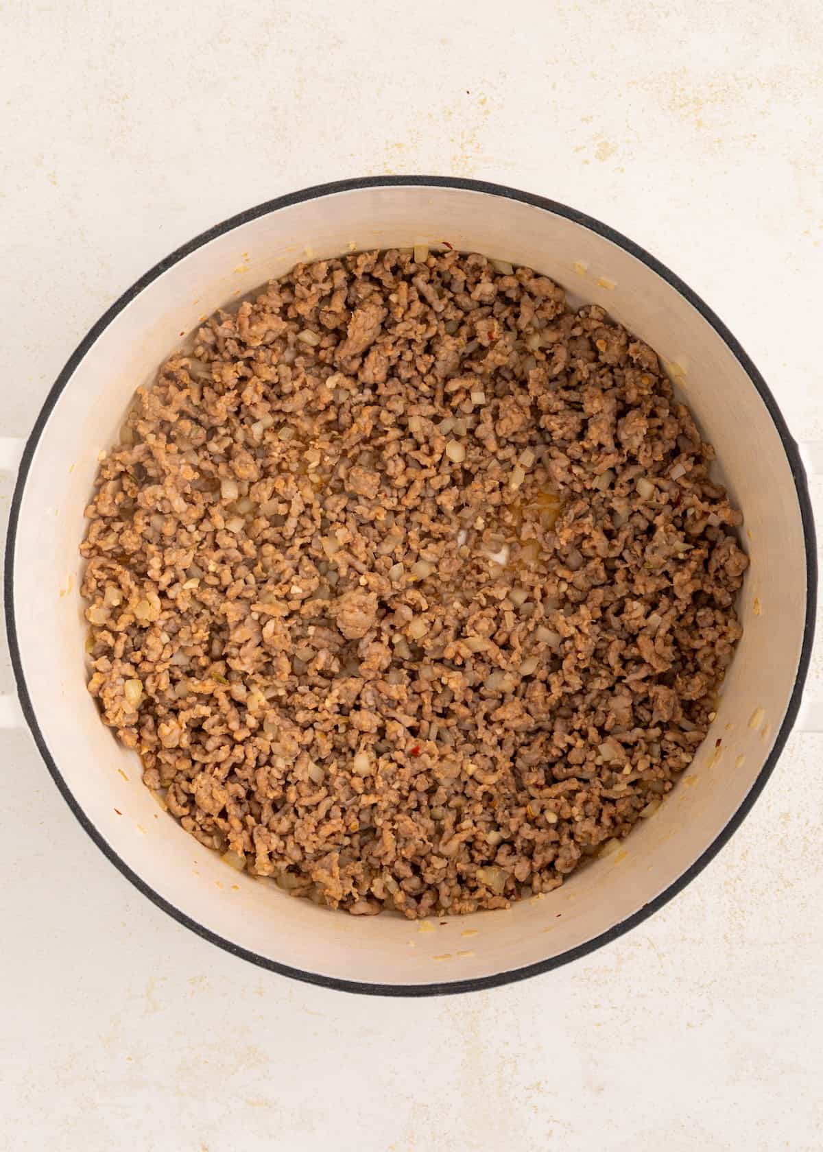 Cooked ground beef and onions in a large white pot, viewed from above.