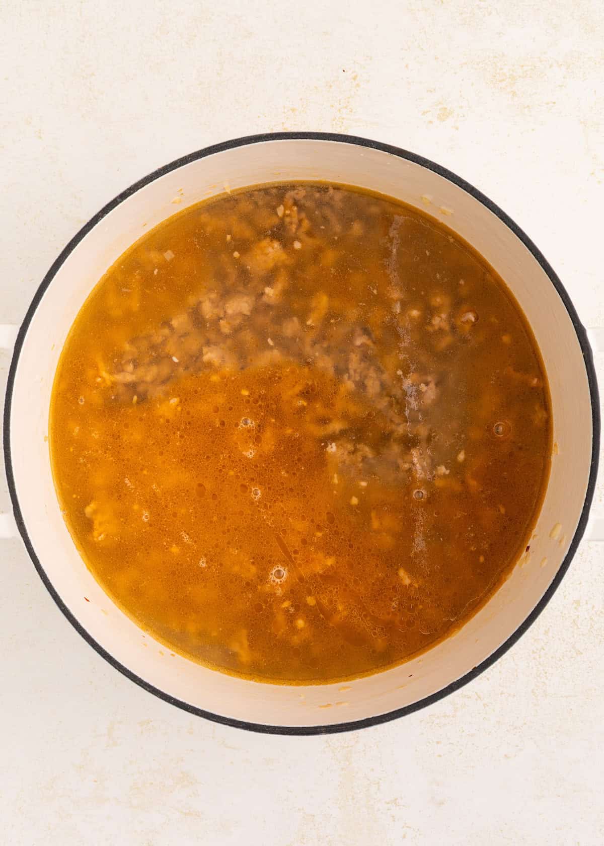 A pot of brown soup with ground meat simmering on a light-colored surface.