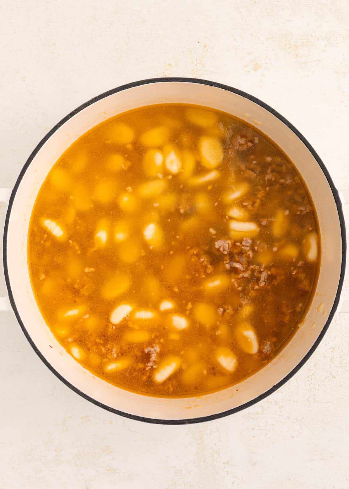 A pot of soup with beans, ground meat, and broth seen from above.