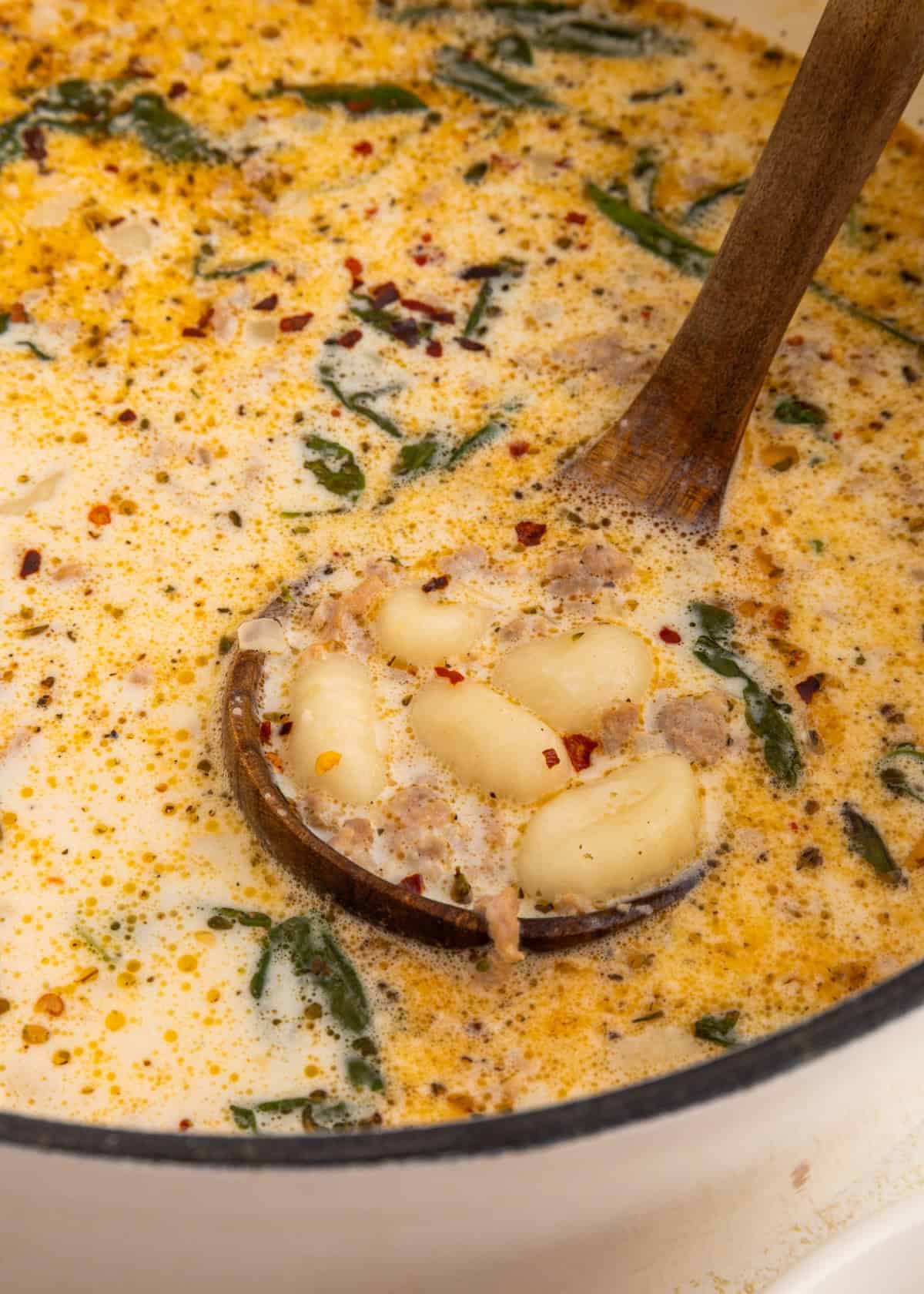 Creamy soup with gnocchi, spinach, and spices being stirred with a wooden ladle.