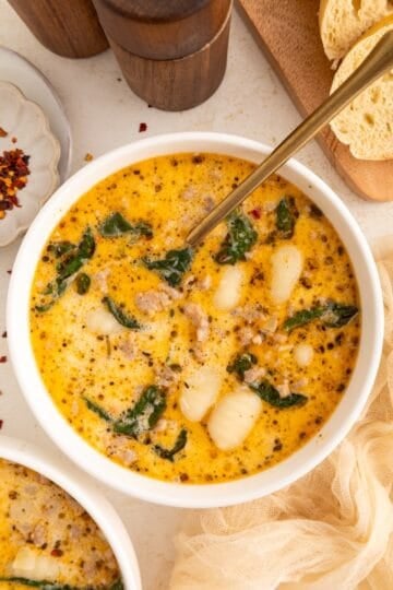 Creamy soup with sausage, gnocchi, and spinach in a white bowl with a gold spoon.