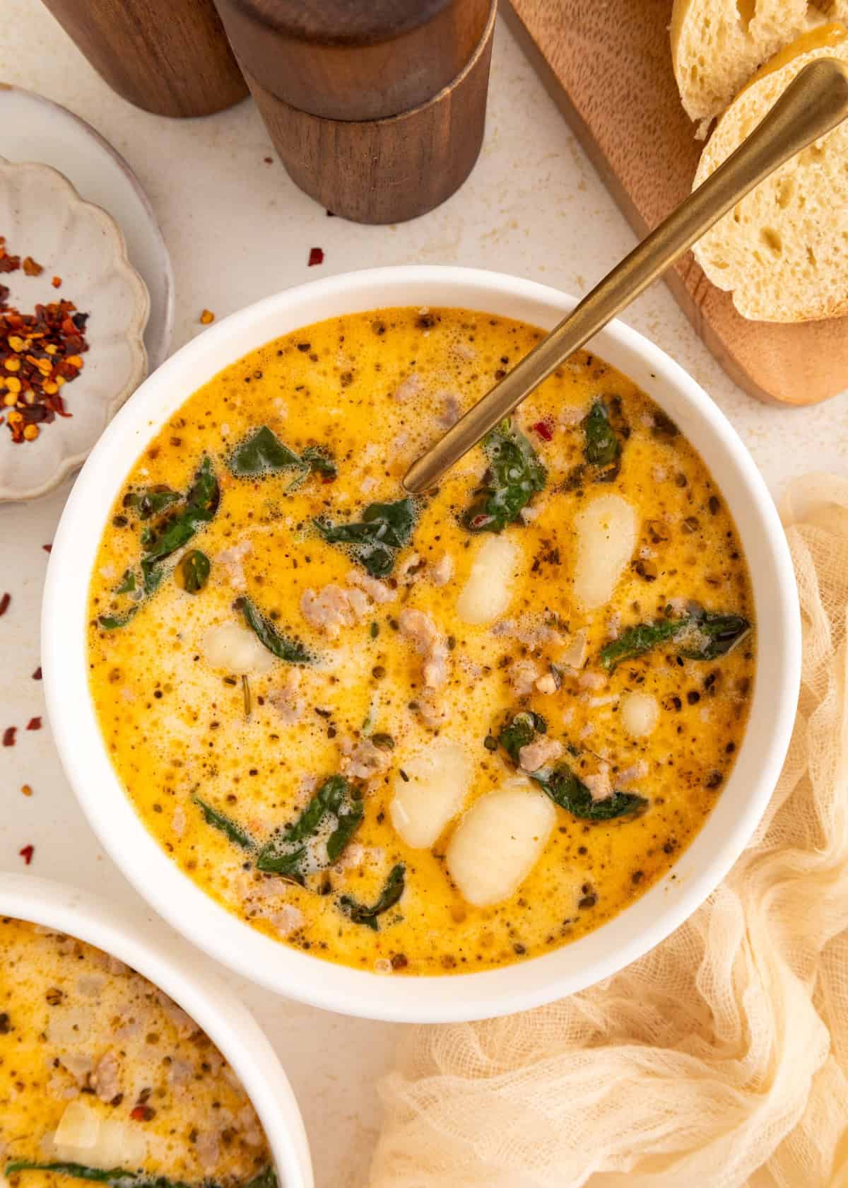 Creamy soup with sausage, gnocchi, and spinach in a white bowl with a gold spoon.