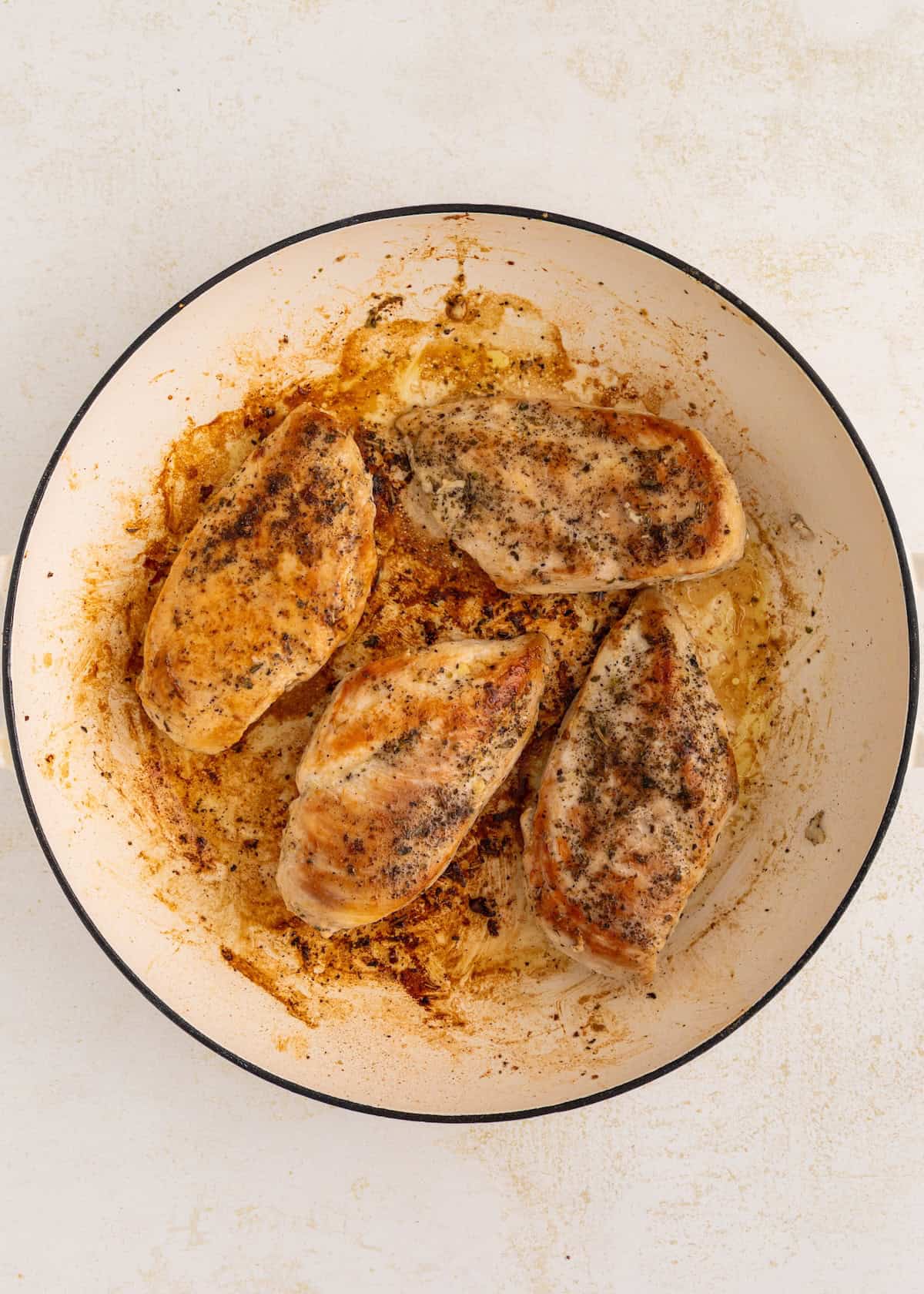 Four seasoned, cooked chicken breasts in a white pan with browned bits on the bottom.