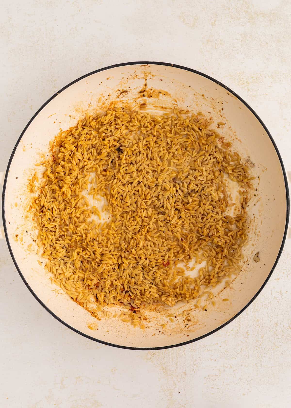 Cooked seasoned rice spread out in a large white skillet on a light surface.