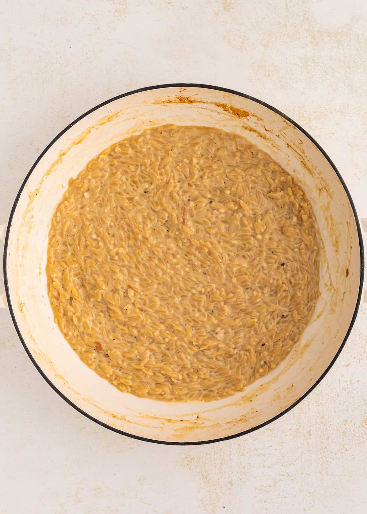 Creamy orzo pasta in a white pot on a light surface.