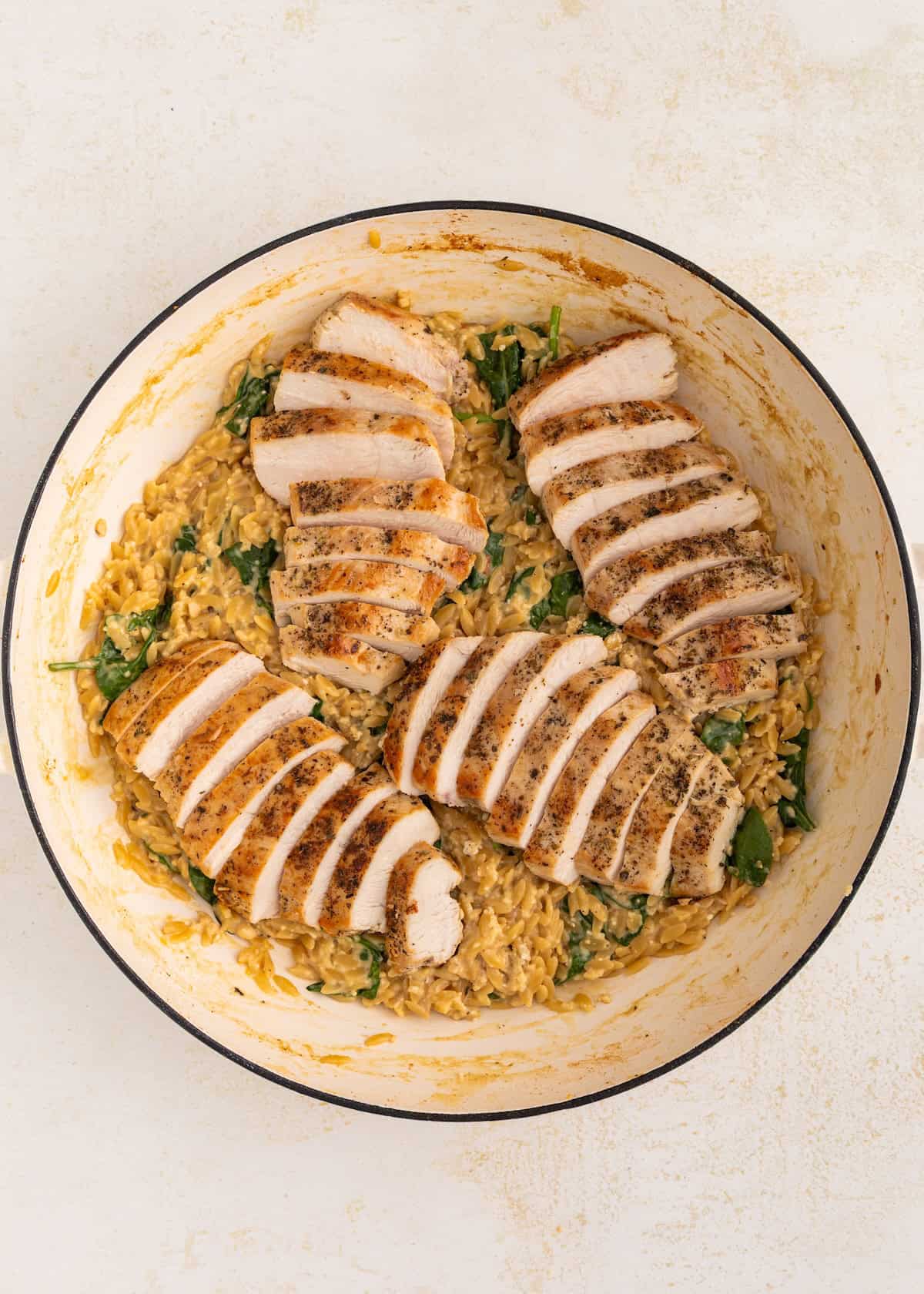 Sliced cooked chicken breast on creamy spinach rice in a white pot.