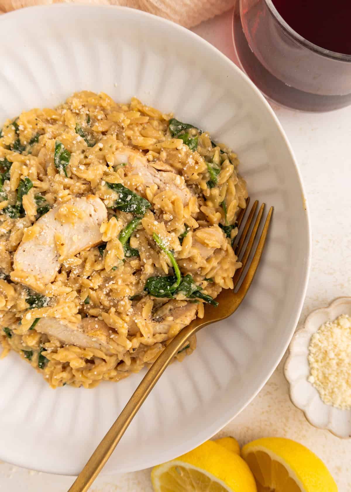 A bowl of creamy orzo with chicken, spinach, and parmesan, served with a glass of red wine.