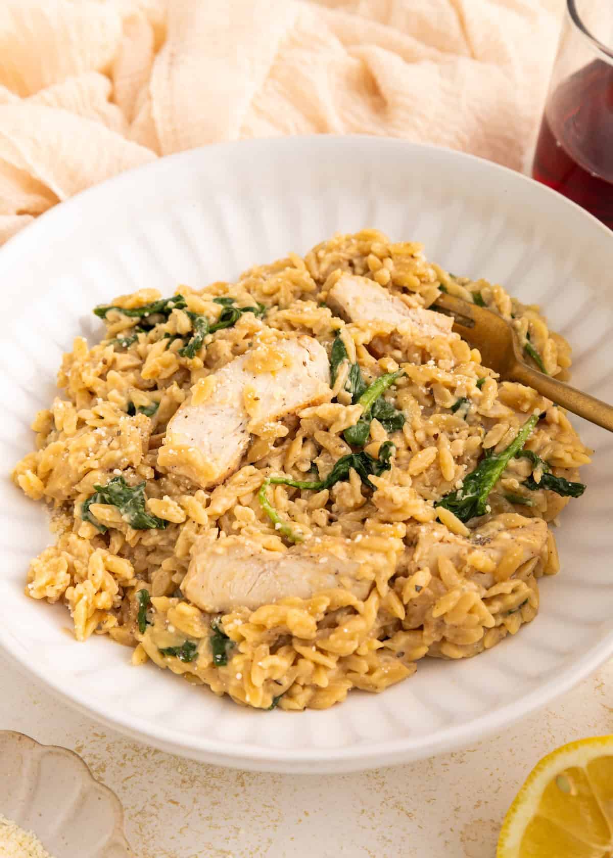 Creamy orzo pasta with spinach and grilled chicken in a white bowl, garnished with cheese.