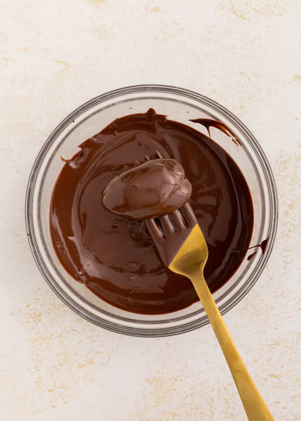 A fork coated in melted chocolate is held over a bowl of melted chocolate.