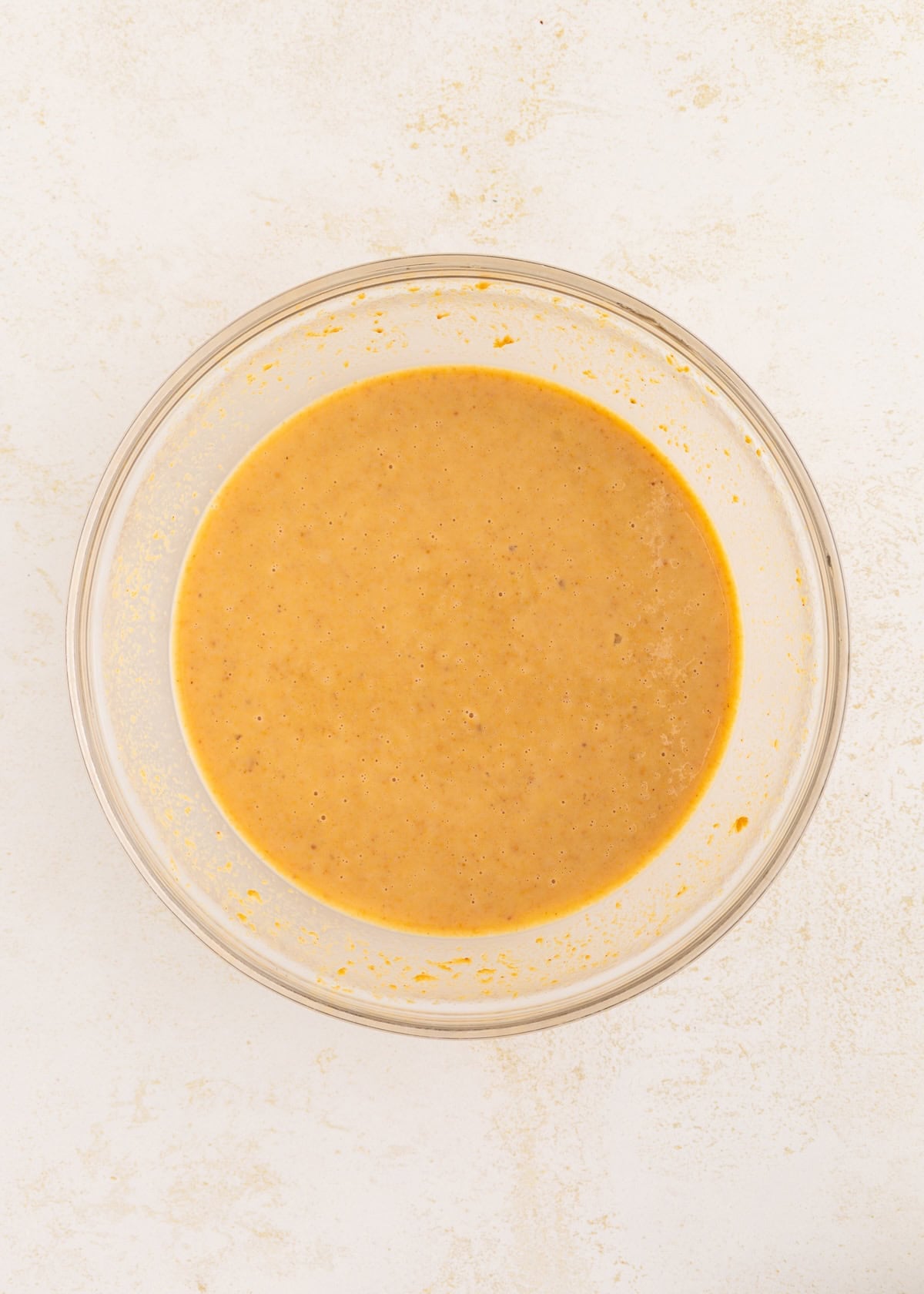 Glass bowl filled with smooth, orange batter on a light, textured surface.
