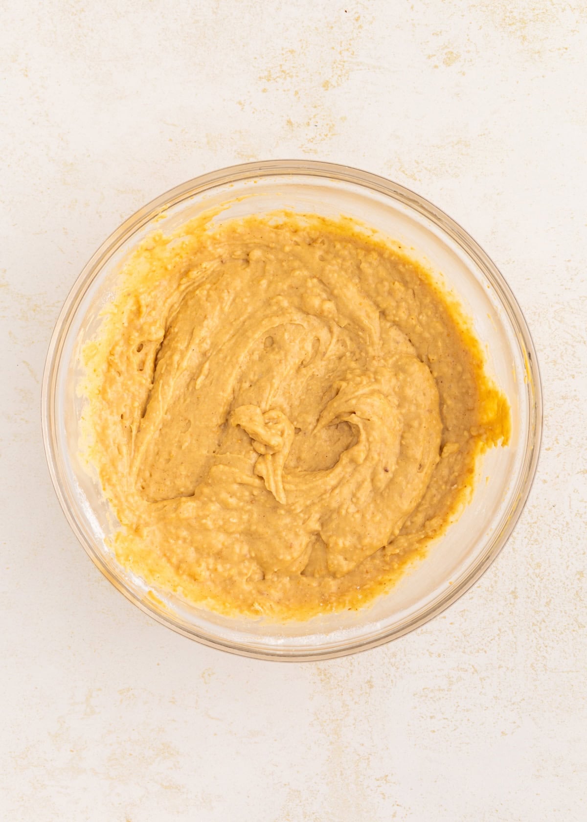 A glass bowl filled with thick, creamy batter on a light-colored surface.