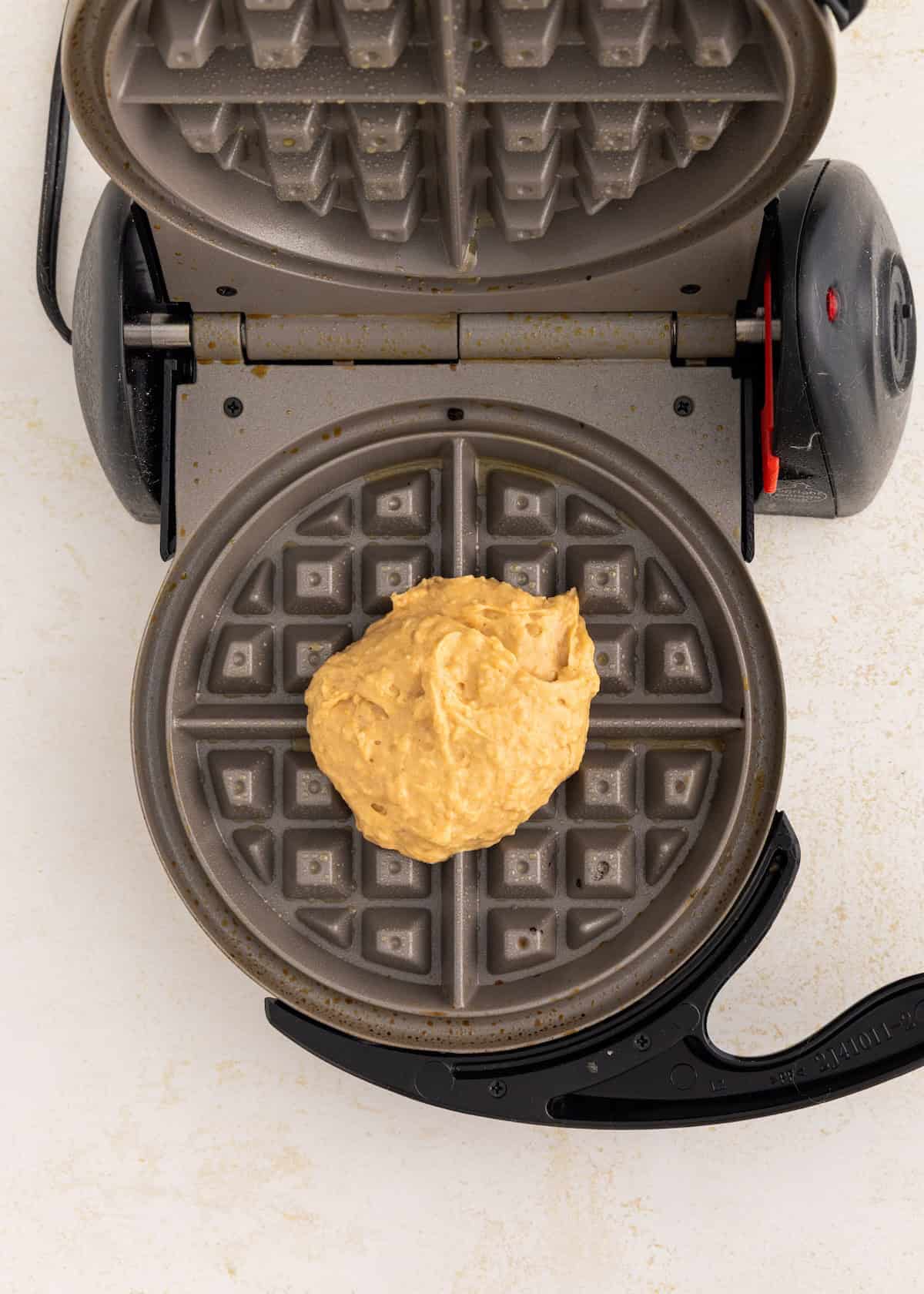 Waffle maker with a scoop of batter in the center, ready to be cooked.