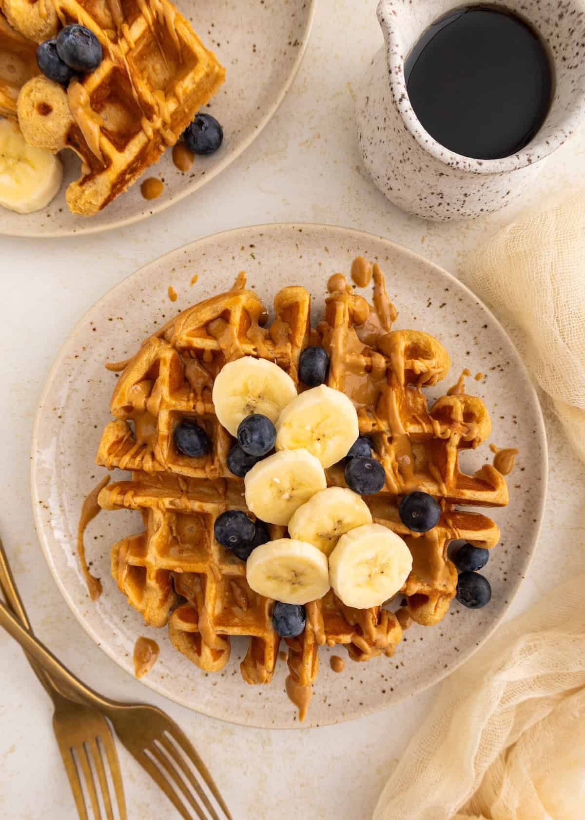 Waffle topped with banana slices, blueberries, and drizzled syrup on a plate.