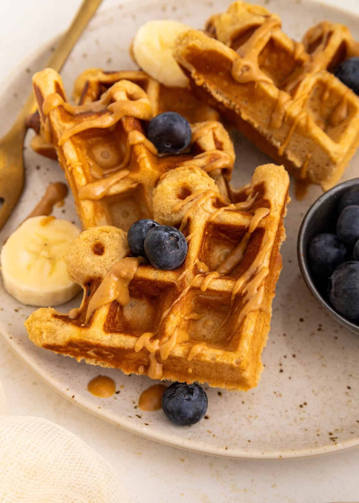 Waffles topped with blueberries, banana slices, and drizzled peanut butter on a plate.