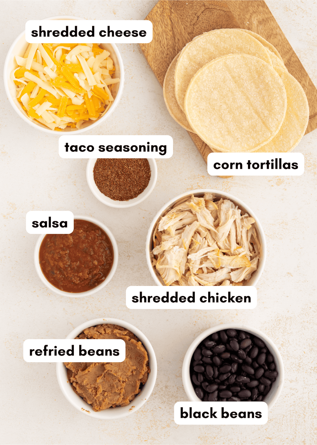 Bowls of shredded cheese, taco seasoning, salsa, shredded chicken, refried beans, black beans, tortillas.