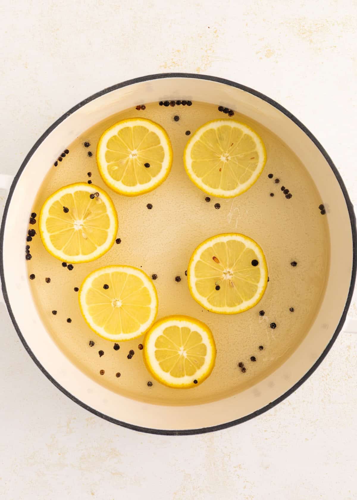 Pot of water with lemon slices and black peppercorns floating on the surface.