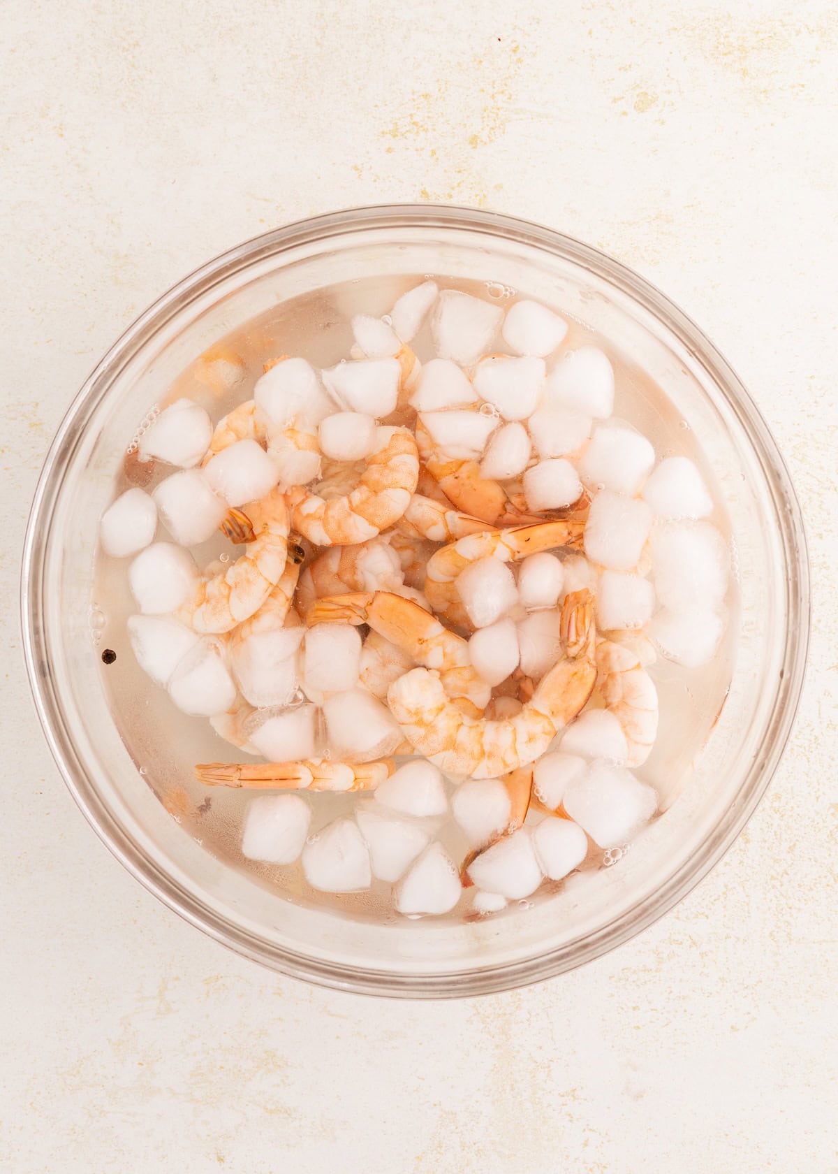 Cooked shrimp in a glass bowl filled with ice water and ice cubes.