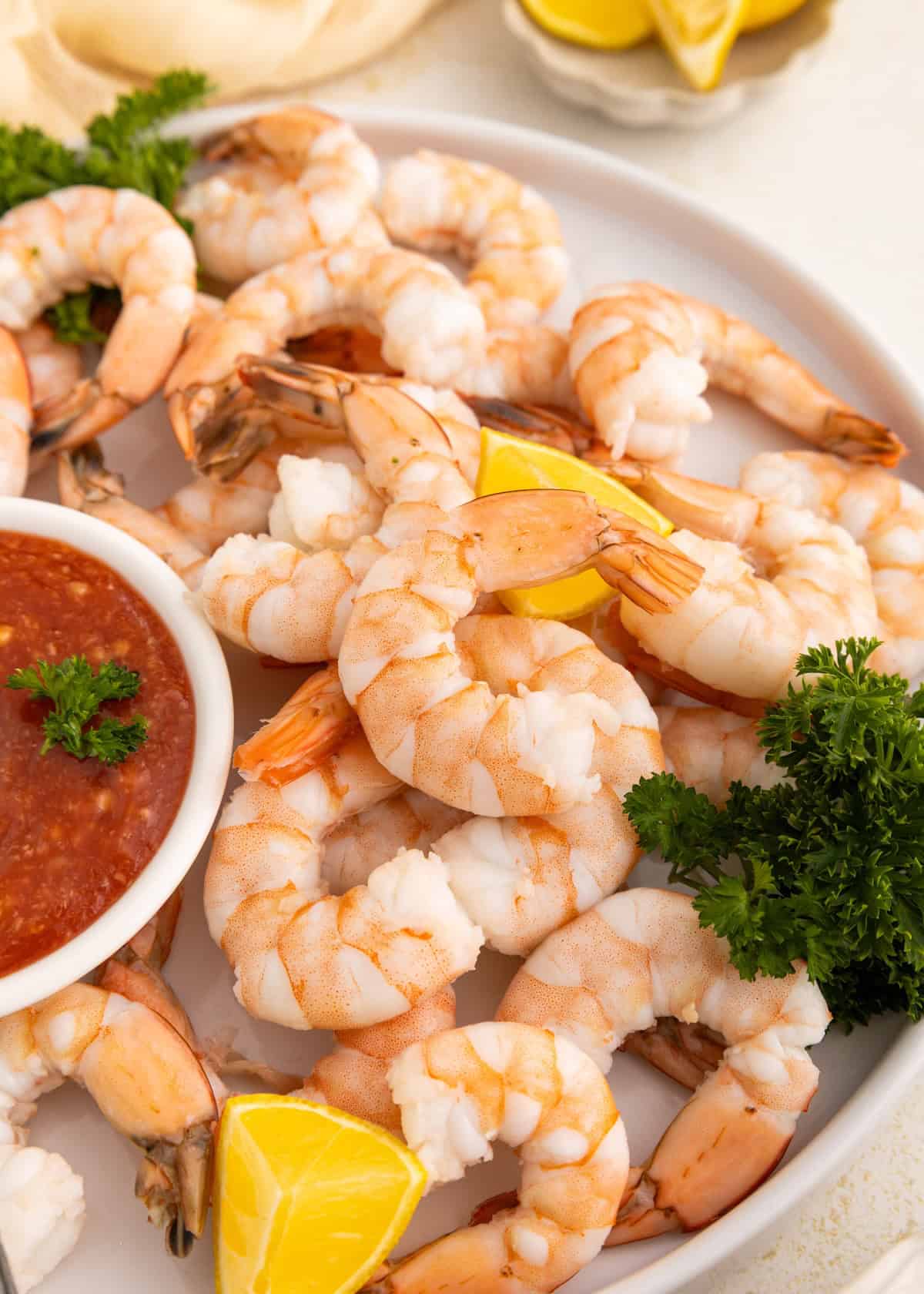 Plate of shrimp cocktail with lemon wedges, parsley, and a bowl of red dipping sauce.