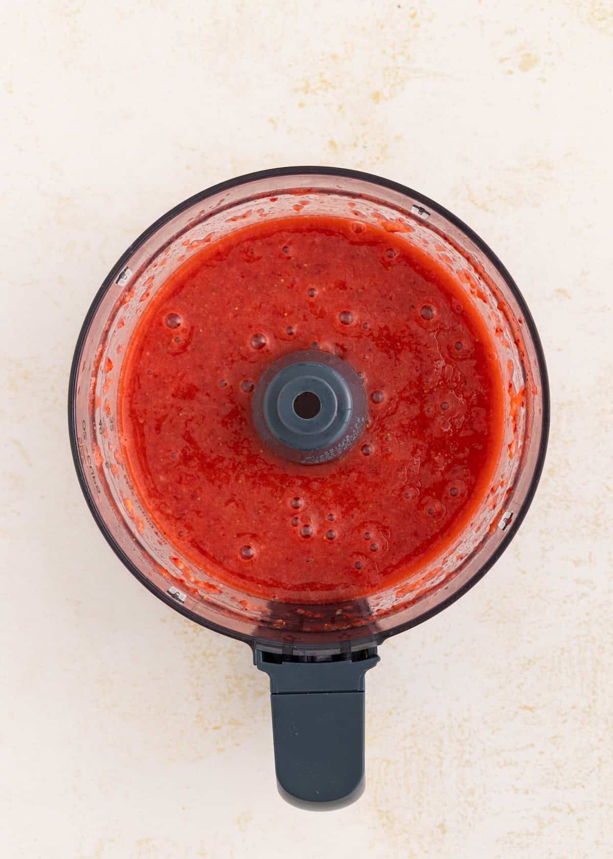 Top view of a food processor bowl filled with blended red strawberry puree.
